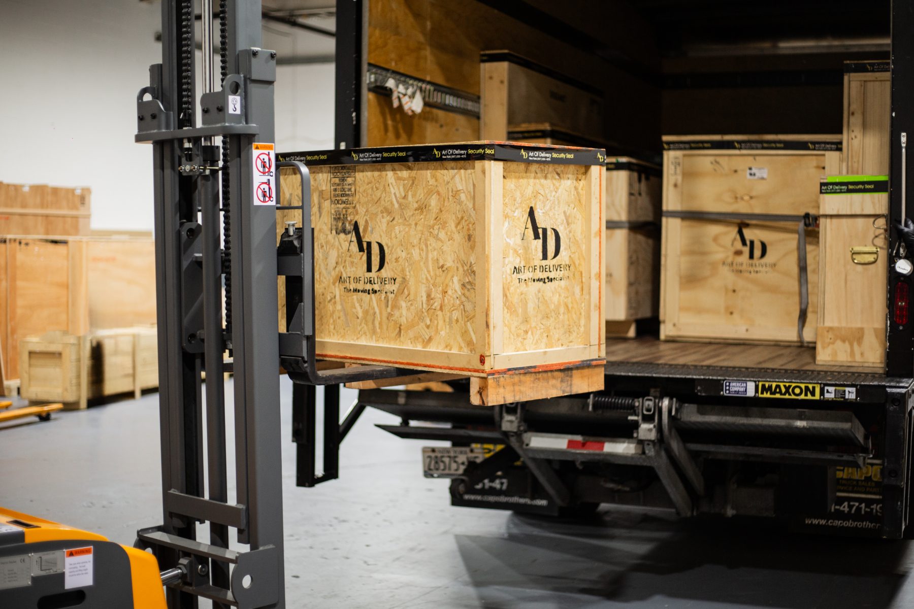 Forklift loading a branded Art of Delivery crate onto the truck