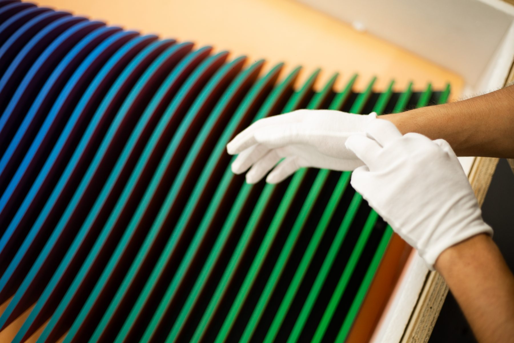 White-gloved hands adjusting a multicolored kinetic artwork